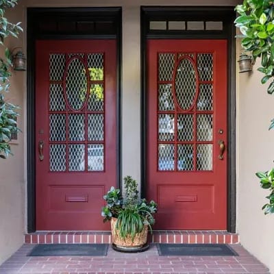 Two red fiberglass front doors with plants on a brick facade